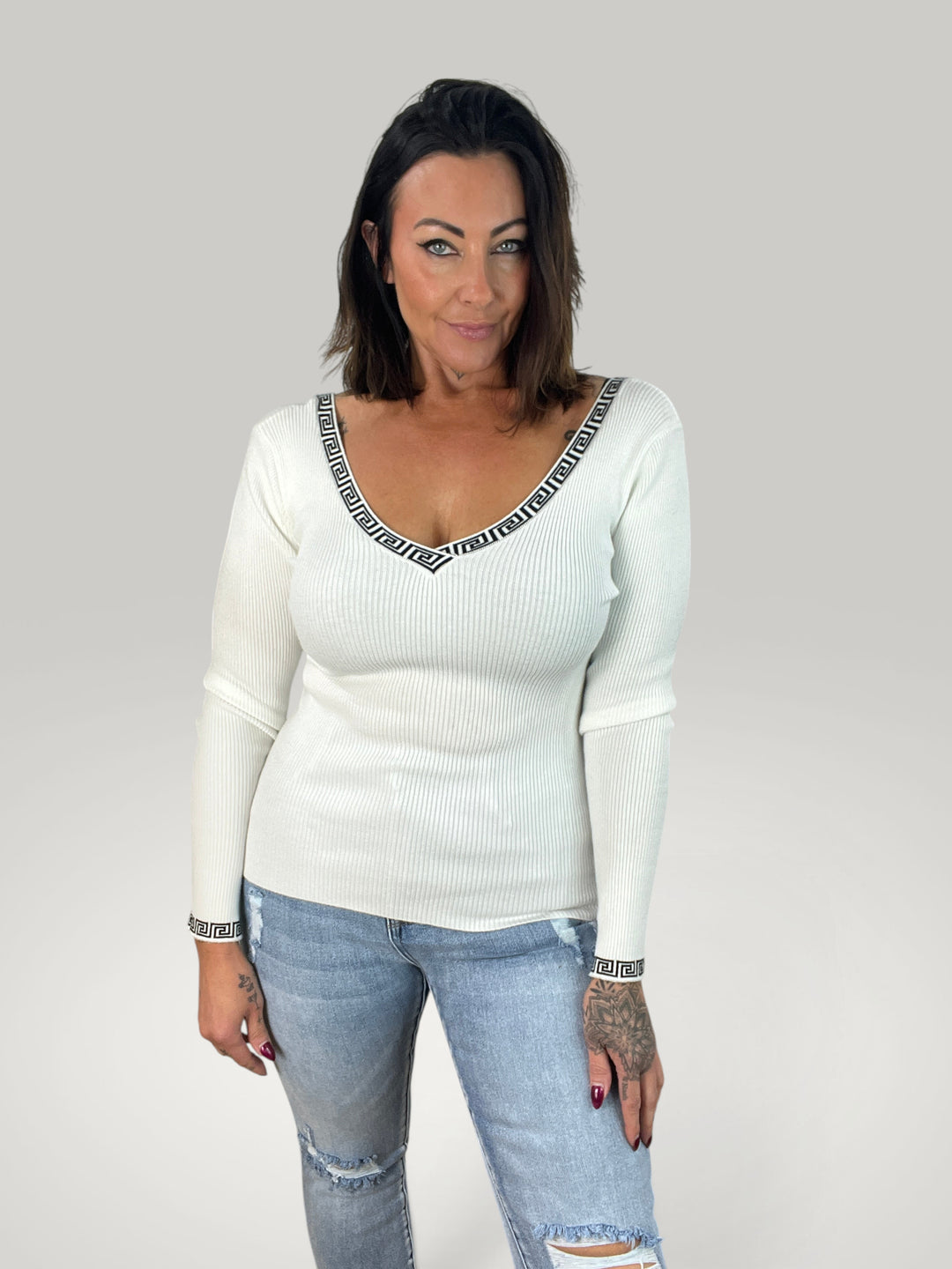 Modelo veste blusa Isabelle Hannover branca de malha canelada com decote em V e detalhe de padrão grego nos punhos