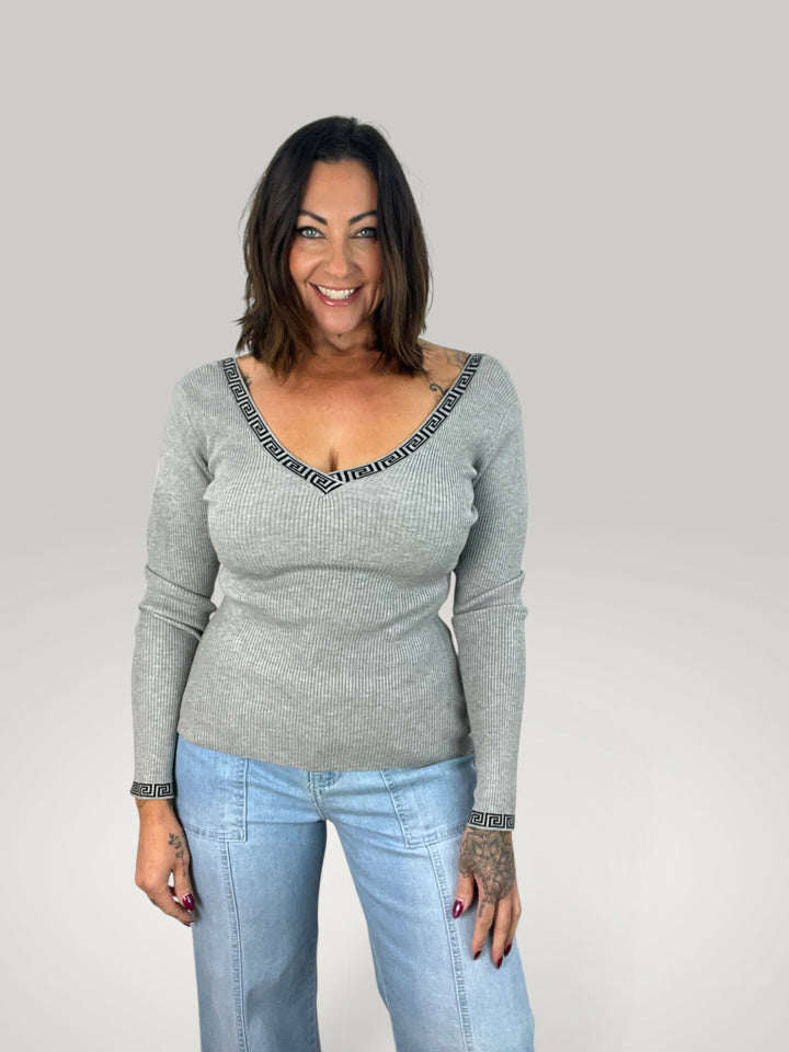 Modelo veste blusa cinzenta Isabelle Hannover com decote em V, detalhe de padrão grego e mangas compridas ajustadas.