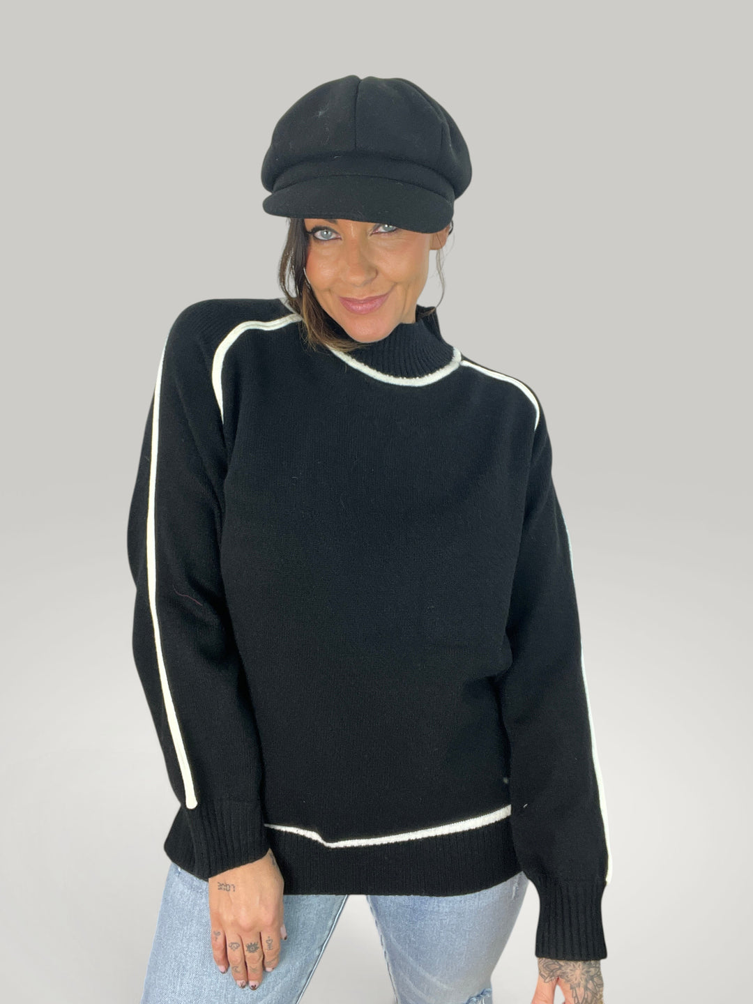 Modelo veste camisola de gola alta preta Isabelle Hannover com detalhes em contraste branco e boné estilo marinheiro.