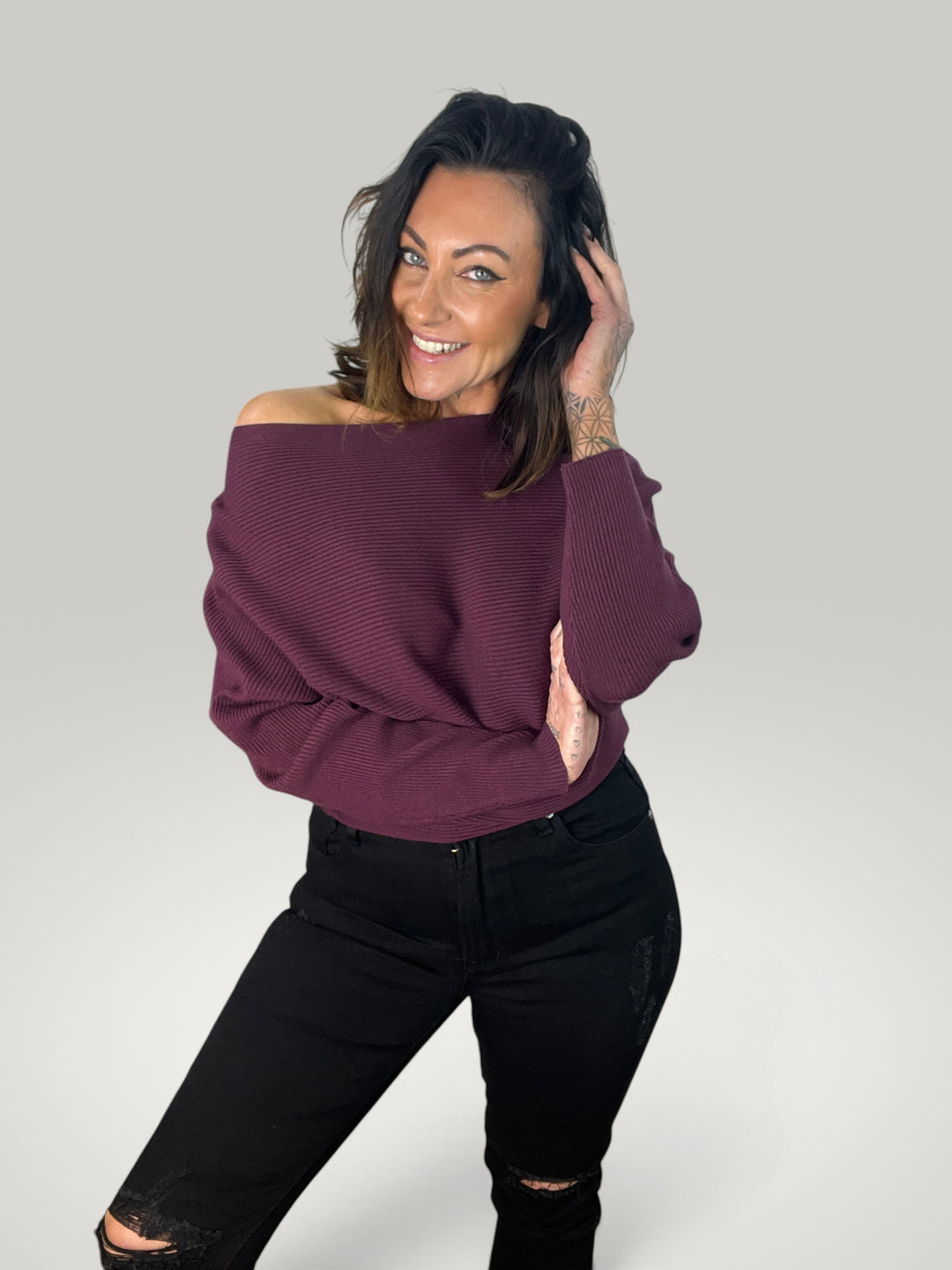 Modelo sorridente veste camisola de malha Isabelle Hannover bordeaux com decote barco e mangas morcego