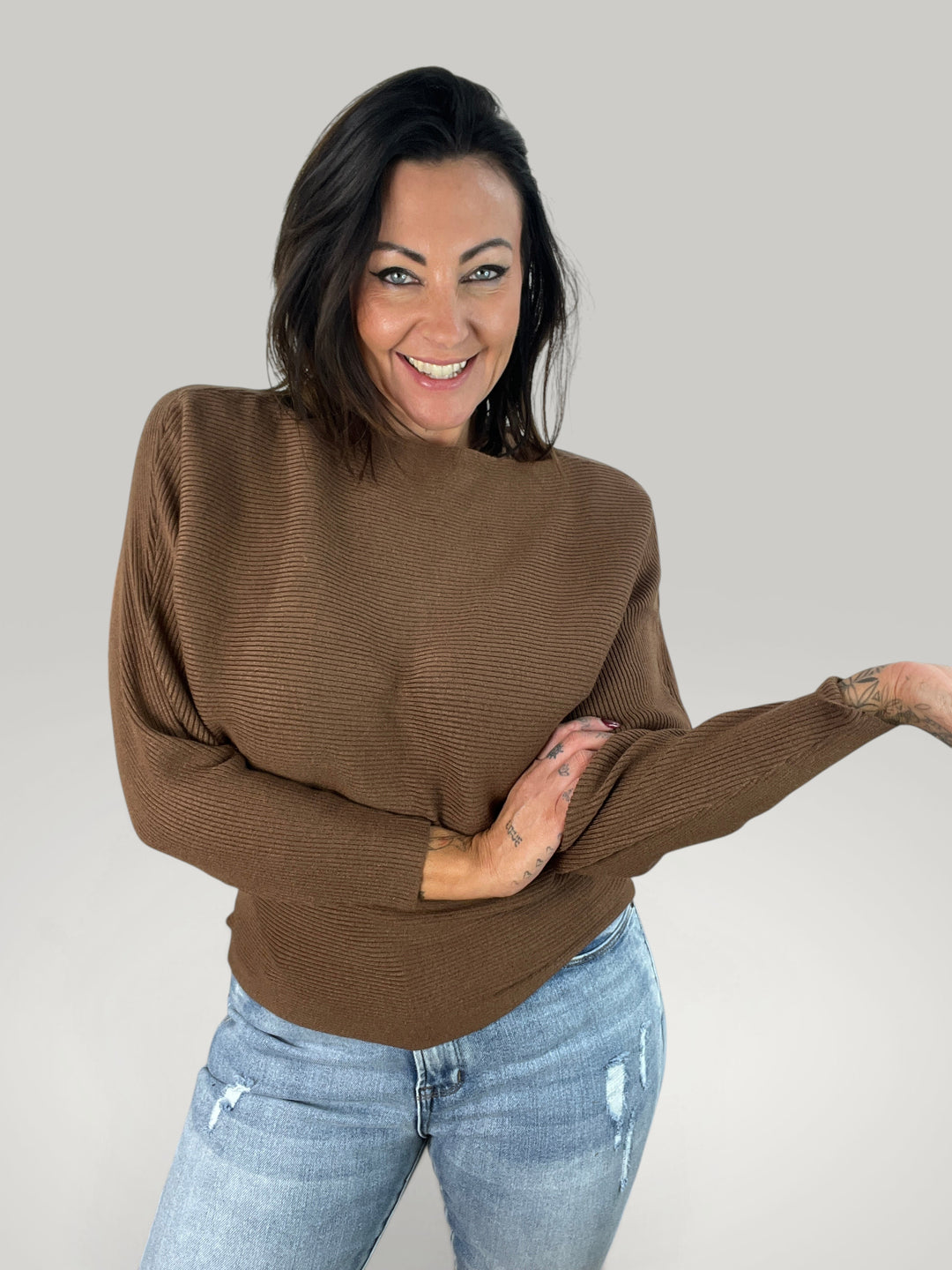 Modelo sorridente veste camisola de malha castanha Isabelle Hannover com decote barco e mangas morcego