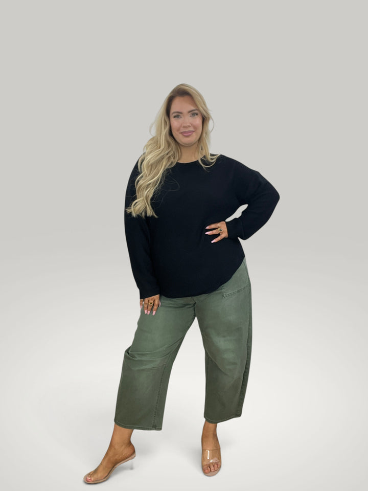 Modelo loira veste camisola de malha preta Isabelle Hannover com gola redonda e bainha assimétrica com calças verdes