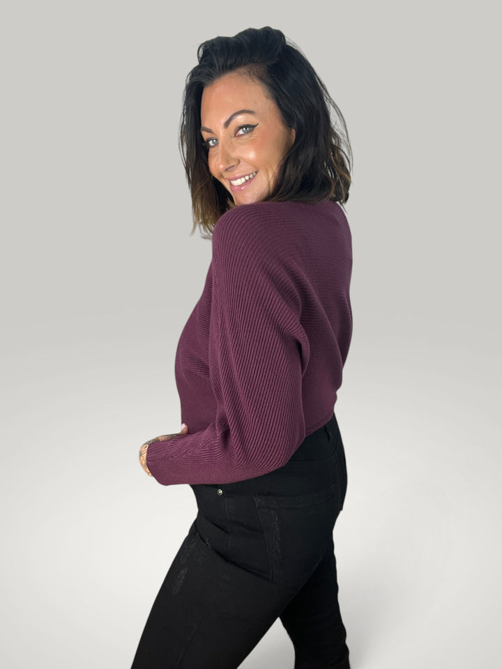 Modelo sorridente Isabelle Hannover veste camisola de malha roxa com decote barco e mangas morcego