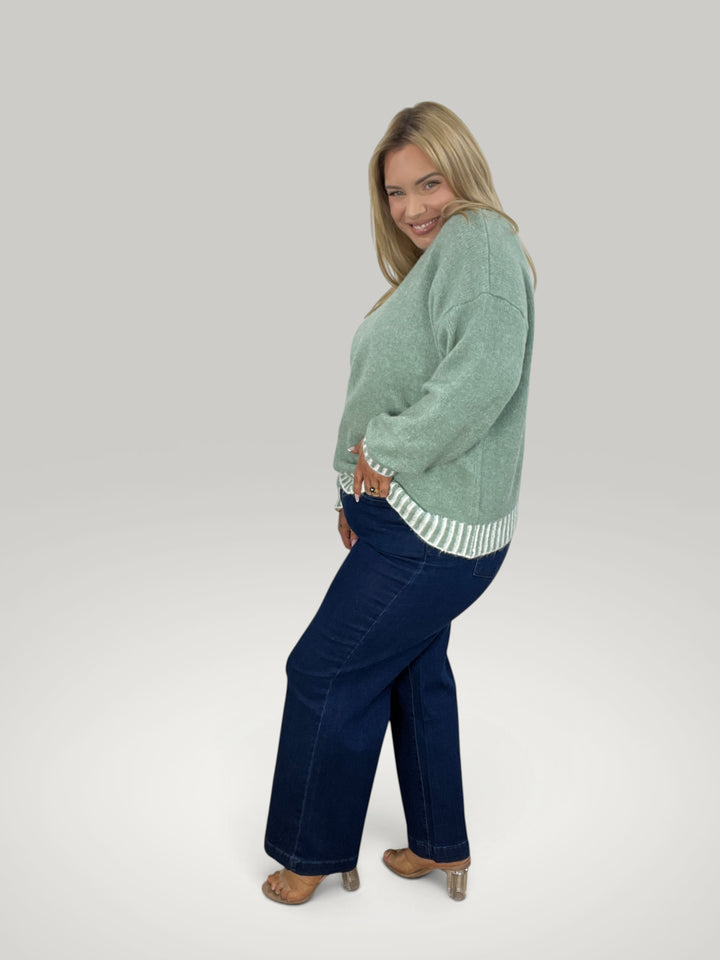 Modelo sorridente veste camisola de malha verde Isabelle Hannover com riscas contrastantes e corte descontraído