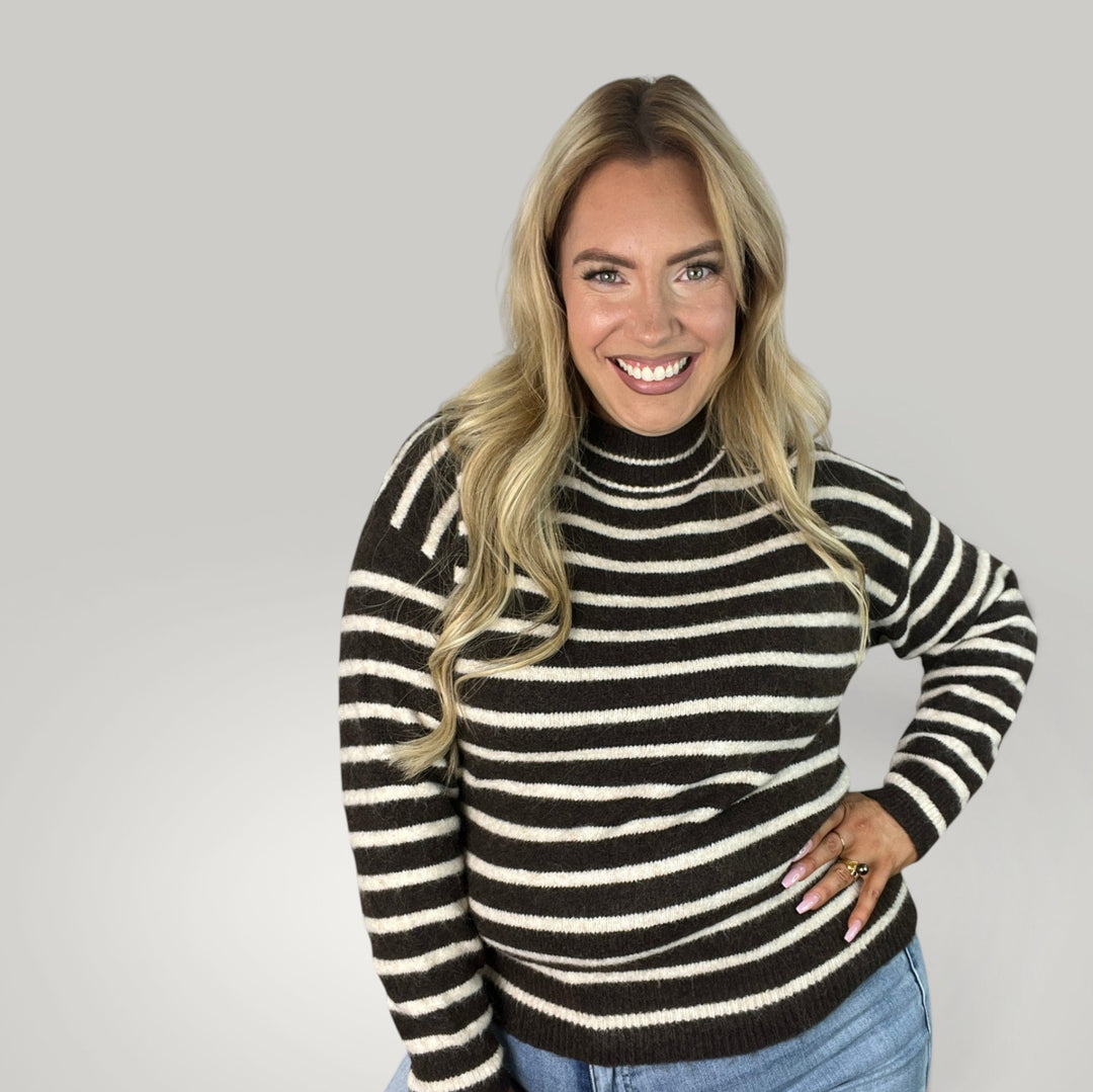 Mulher loira sorridente a usar camisola de malha às riscas com gola alta da marca Isabelle Hannover