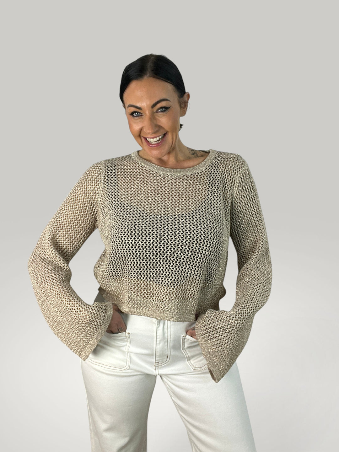 Modelo sorridente veste Isabelle Hannover crop top de crochê bege com mangas sino e gola redonda canelada