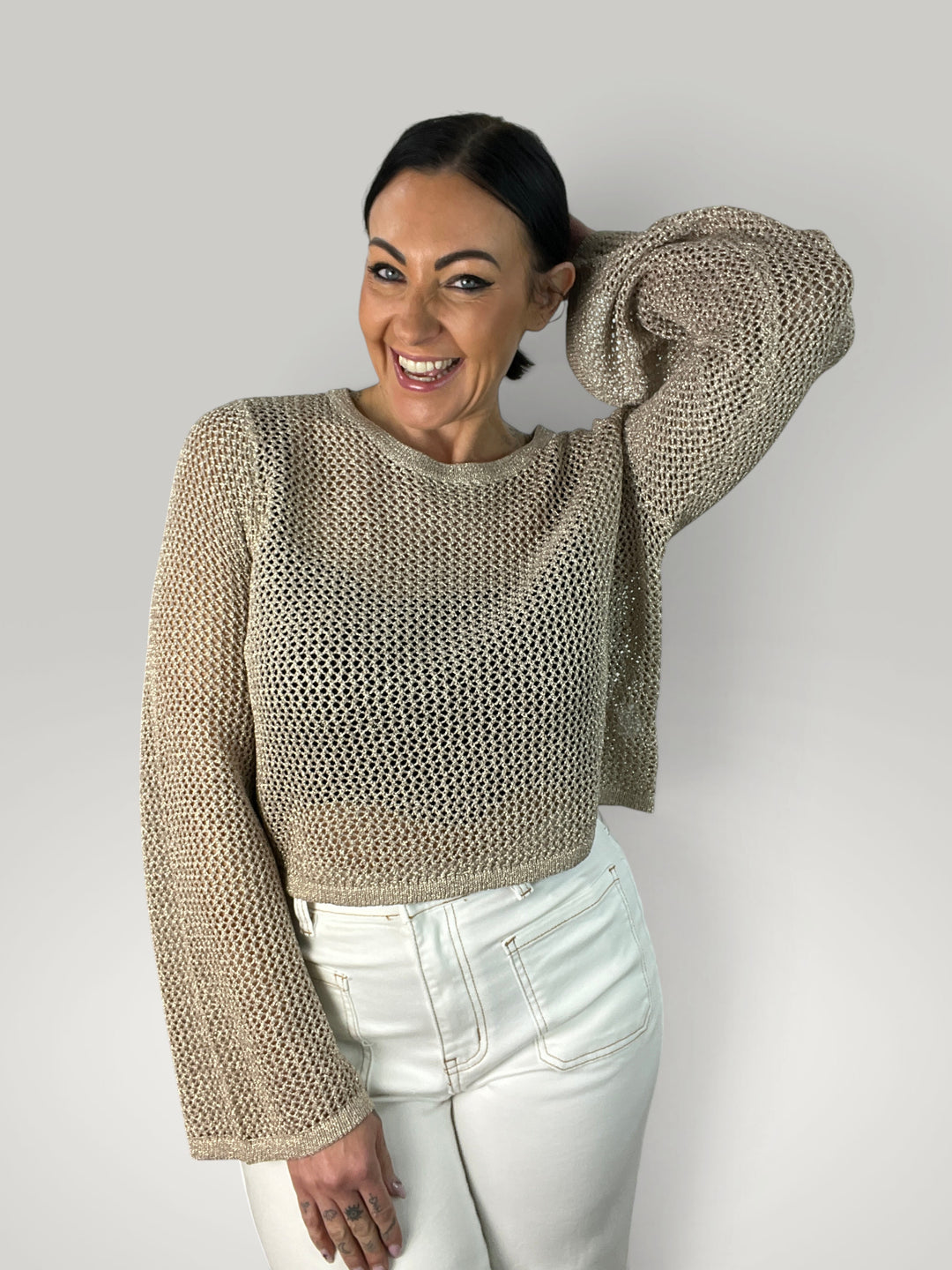 Modelo sorridente veste crop top de crochê bege da Isabelle Hannover com mangas sino e gola redonda canelada.