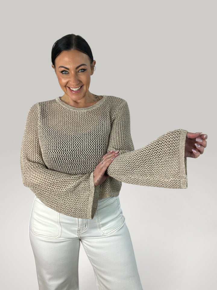 Modelo sorridente veste Isabelle Hannover crop top de croché bege com mangas largas e gola redonda em fundo neutro