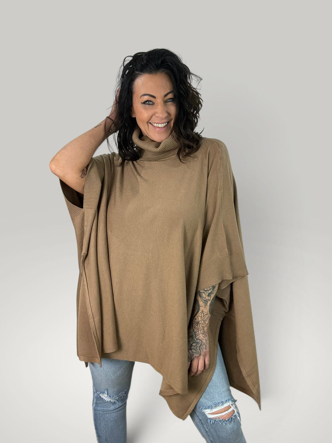 Modelo sorridente veste poncho bege Isabelle Hannover de malha macia com gola alta e corte oversized