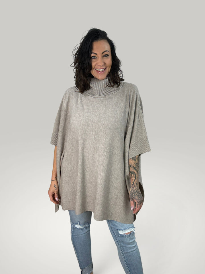Modelo veste poncho bege Isabelle Hannover de gola alta e corte oversized em malha macia com mangas curtas