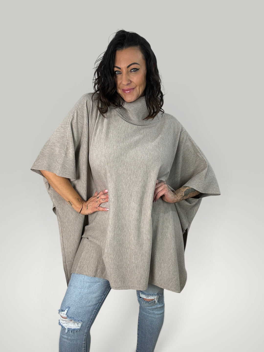 Modelo veste poncho bege oversized Isabelle Hannover com gola alta canelada e mangas curtas em malha macia