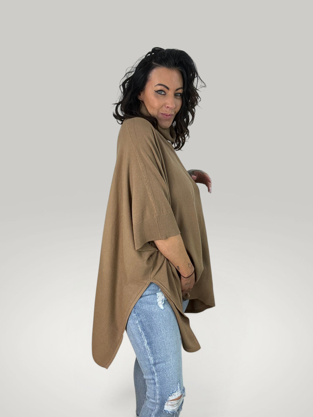 Modelo veste poncho bege Isabelle Hannover com gola alta, corte oversized e mangas curtas em malha macia