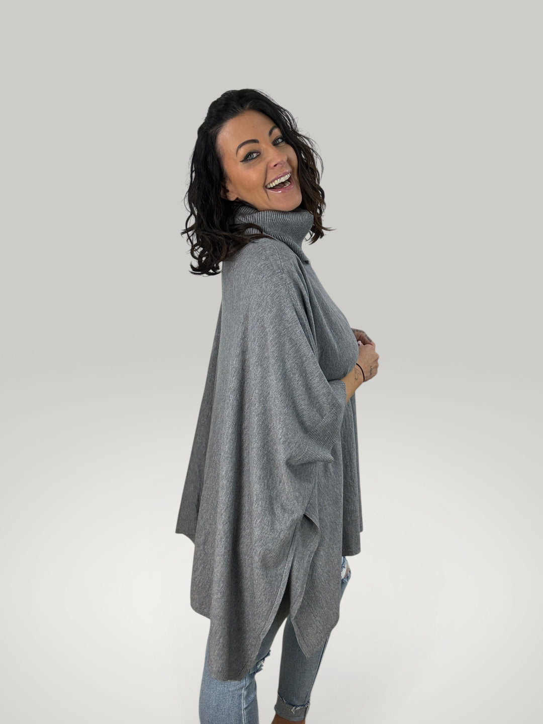Modelo sorridente veste poncho cinzento Isabelle Hannover com gola alta, corte oversized e mangas curtas em malha