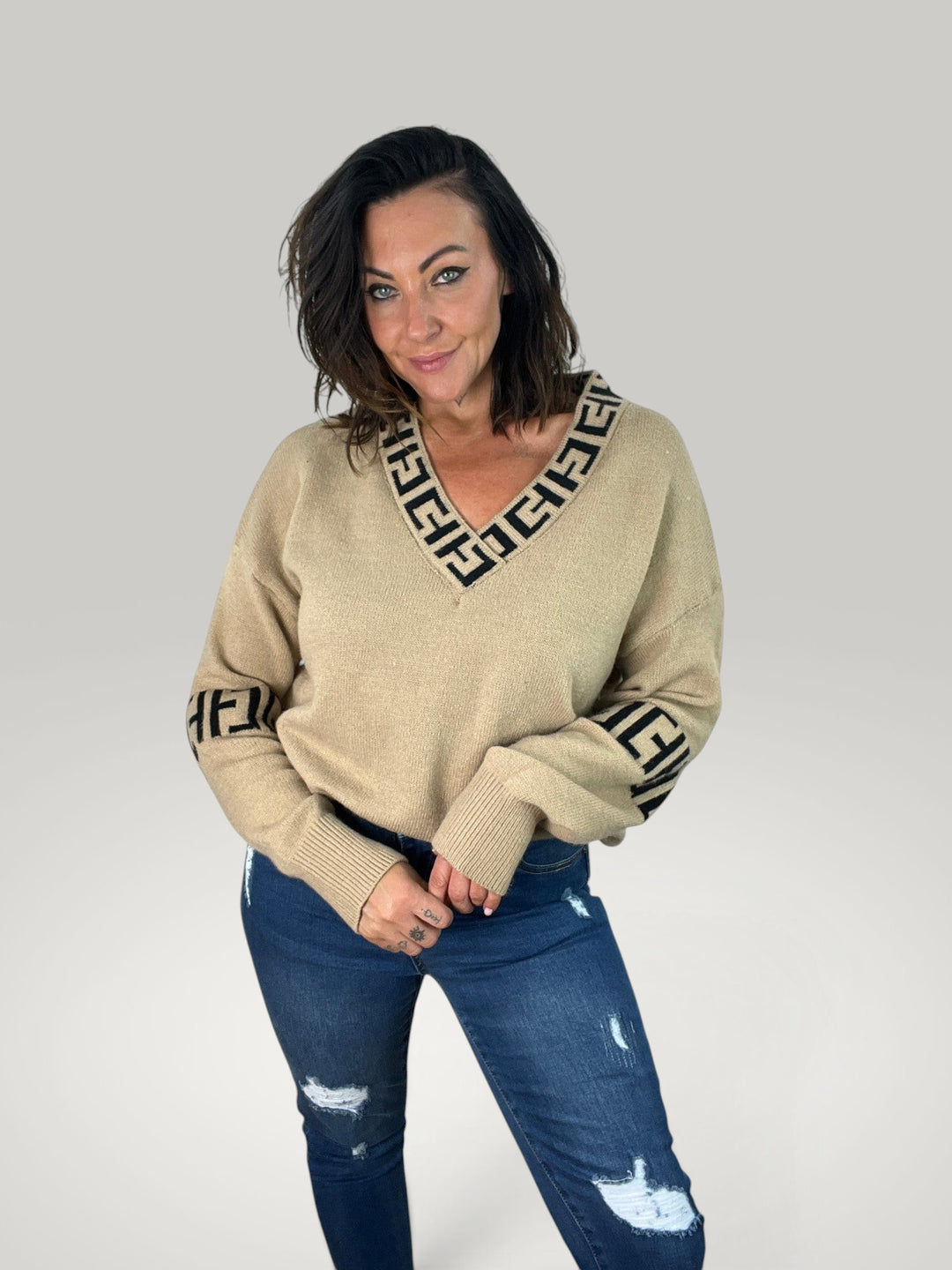 Modelo veste pulôver bege Isabelle Hannover com decote em V, detalhe estampado e mangas compridas em corte relaxado.