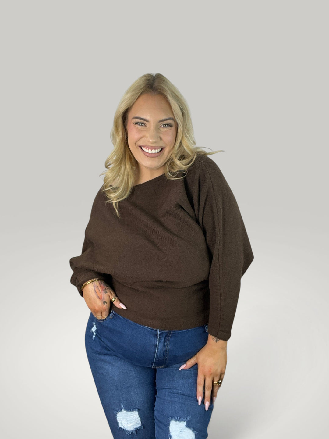 Modelo sorridente veste pulôver castanho Isabelle Hannover com decote barco e mangas 7/8 em algodão macio e elástico.