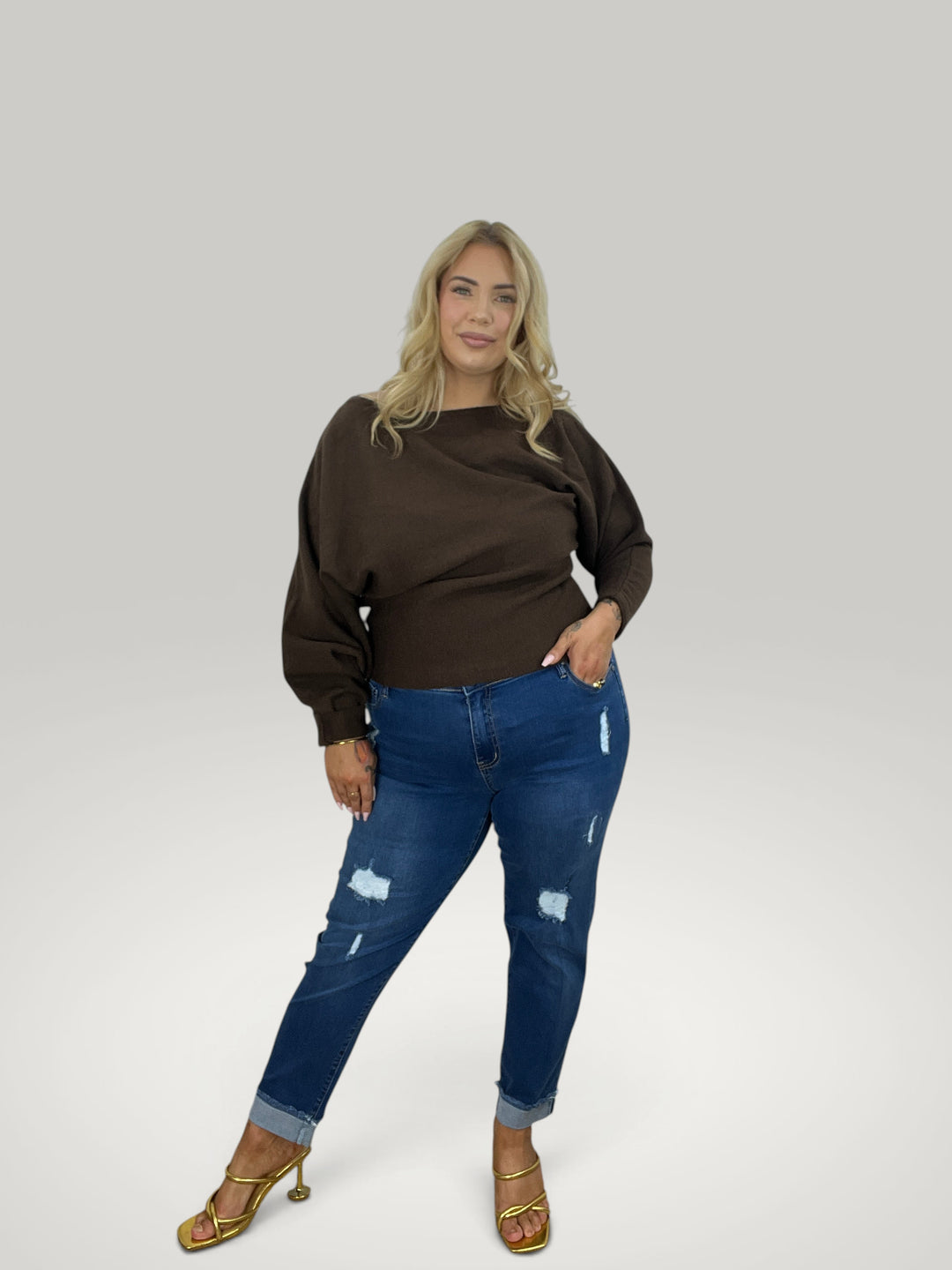 Modelo loira veste pulôver Isabelle Hannover castanho com decote canoa e mangas 7/8, combinado com jeans azul.