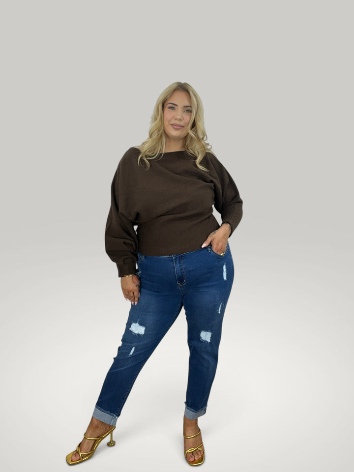 Modelo loira veste pulôver Isabelle Hannover castanho com decote canoa e mangas 7/8, combinado com jeans azul.