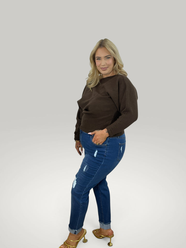 Modelo loira veste pulôver castanho Isabelle Hannover com decote canoa e mangas 7/8, combinado com jeans azul.