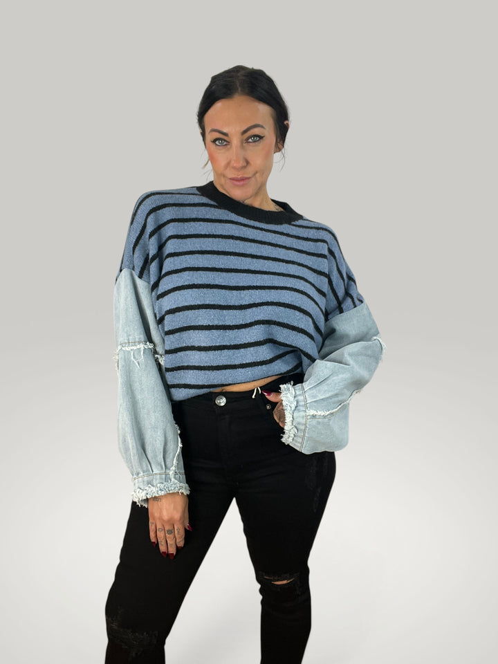 Modelo veste pulôver Isabelle Hannover listrado com mangas de jeans e gola redonda em corte descontraído.