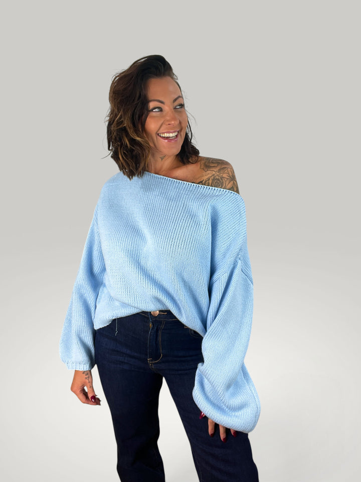 Modelo sorridente veste pulôver de malha azul Isabelle Hannover com corte largo, decote redondo e mangas balão.
