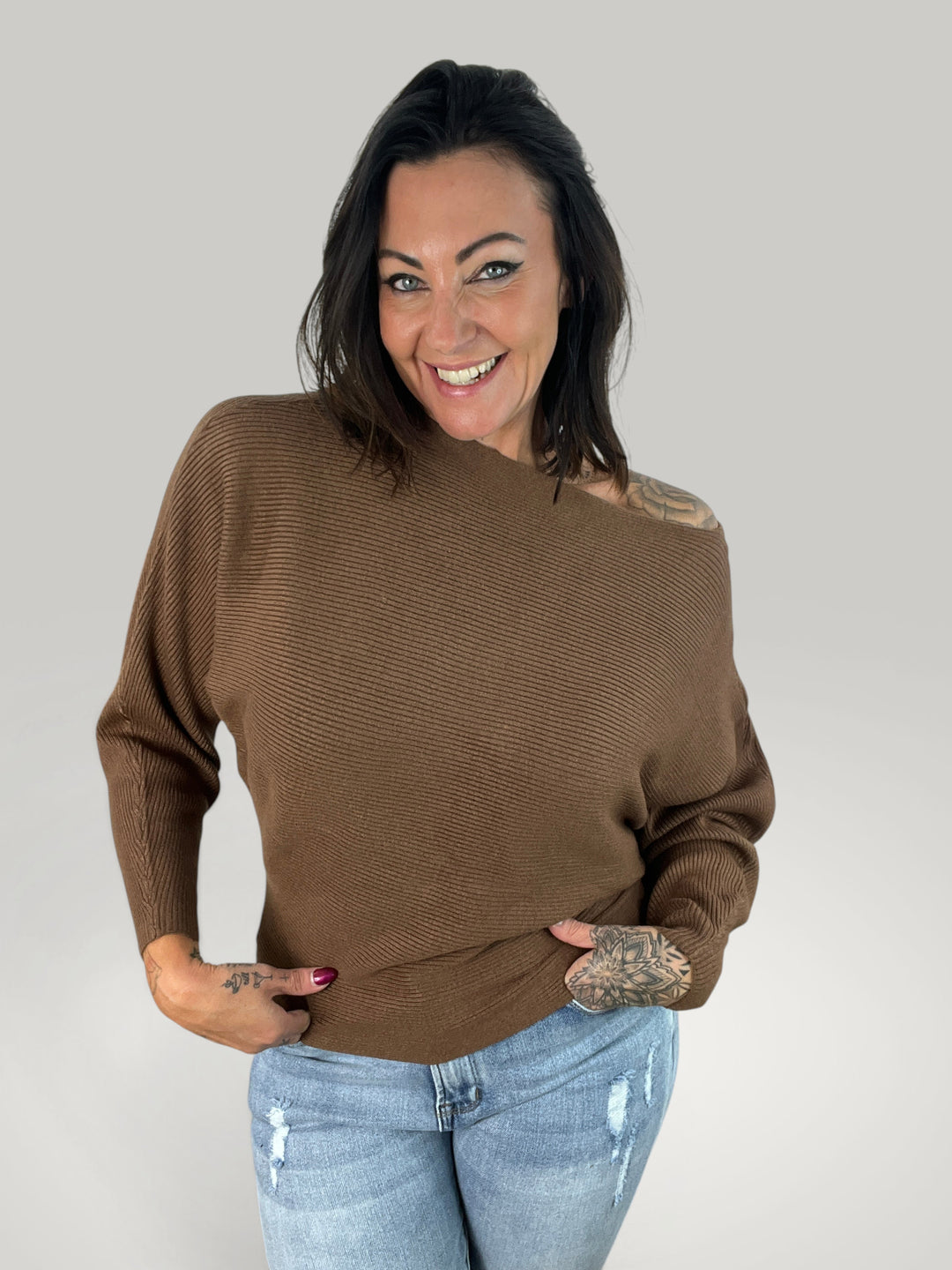 Modelo sorridente veste pulôver de malha castanho Isabelle Hannover com decote canoa e mangas morcego