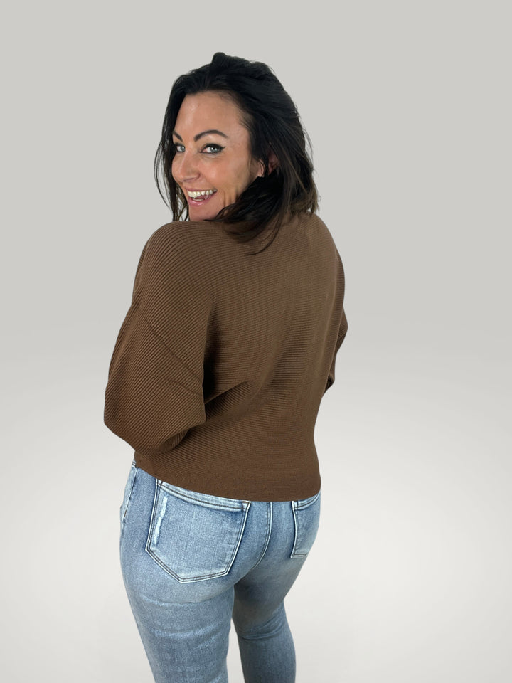 Modelo veste pulôver de malha castanho Isabelle Hannover com corte largo e mangas morcego, vista de costas.