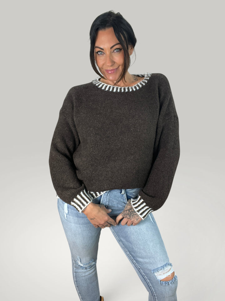 Modelo veste pulôver de malha Isabelle Hannover castanho com riscas contrastantes no decote e punhos, corte casual.