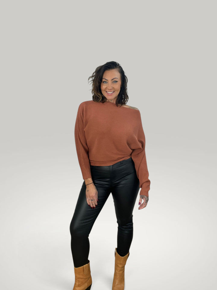 Modelo veste pulôver de malha Isabelle Hannover cor ferrugem com decote canoa e mangas morcego em fundo neutro