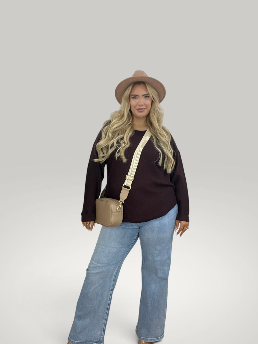 Mulher loira usando pulôver de malha Isabelle Hannover marrom com decote canoa, calça jeans e chapéu bege.
