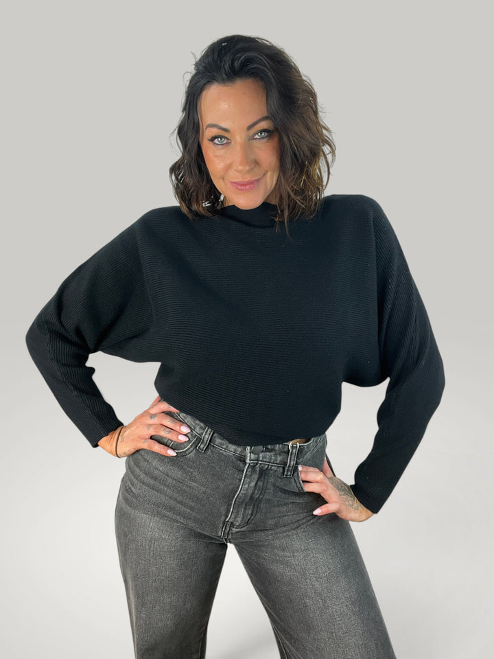 Modelo veste pulôver de malha preto Isabelle Hannover com decote canoa e mangas morcego, estilo casual e elegante.