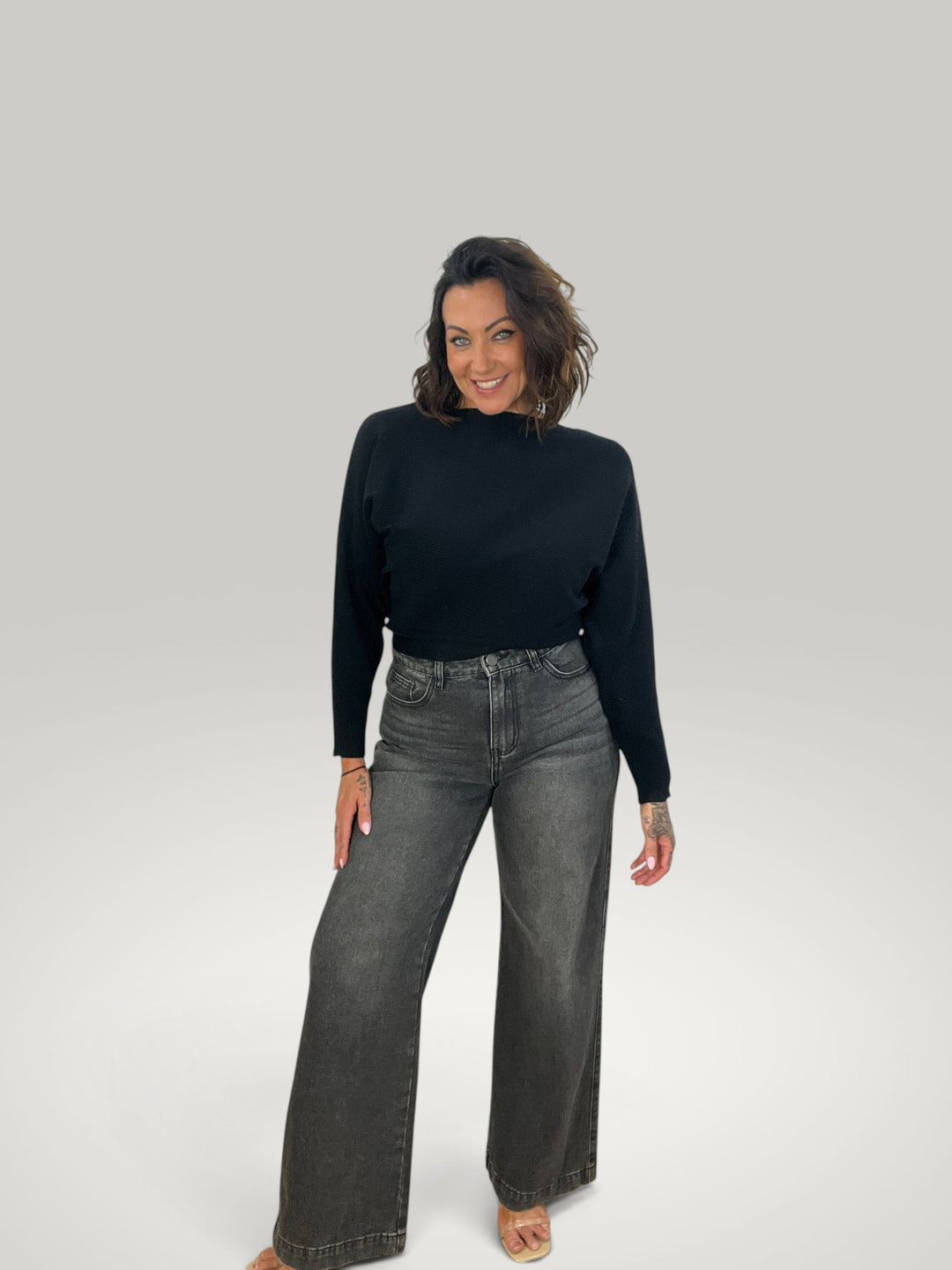 Modelo veste pulôver de malha preto Isabelle Hannover com decote canoa e mangas morcego, combinado com calças jeans