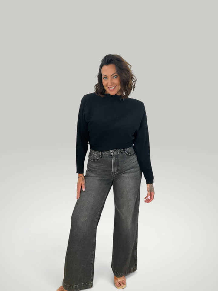 Modelo veste pulôver de malha preto Isabelle Hannover com decote canoa e mangas morcego, combinado com calças jeans