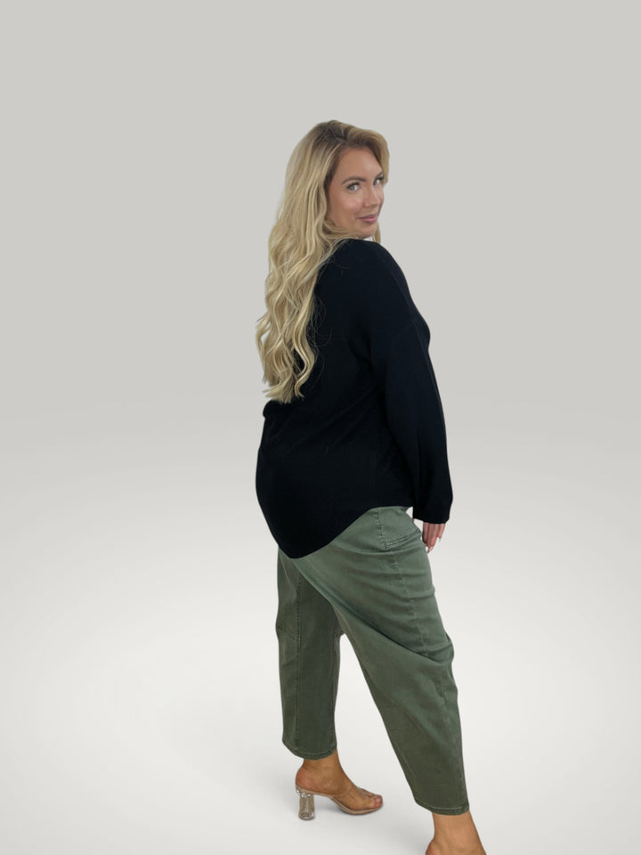 Modelo loira veste pulôver de malha preto Isabelle Hannover com gola redonda e bainha assimétrica sobre calças cáqui