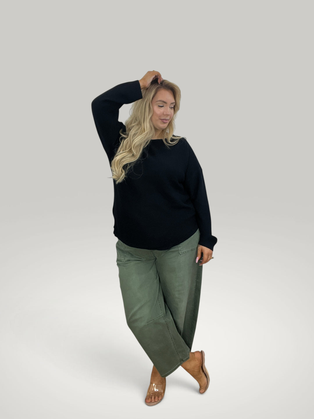 Modelo loira usa pulôver de malha preto Isabelle Hannover com gola redonda e bainha assimétrica e calças verdes