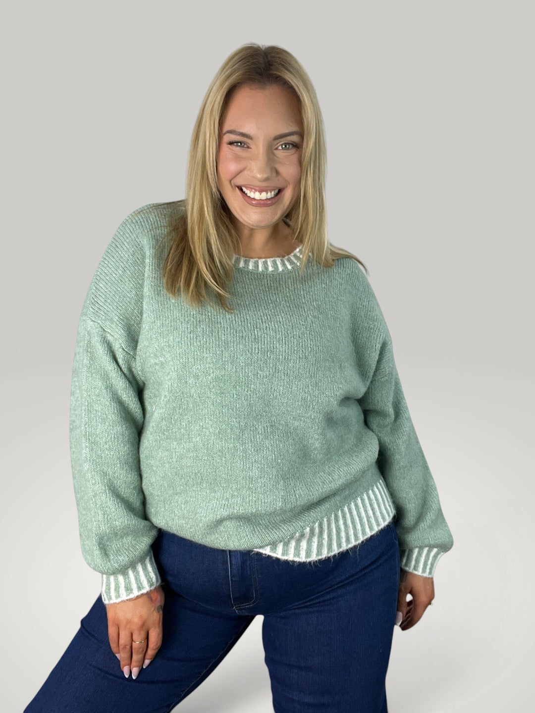 Modelo sorridente veste pulôver de malha verde Isabelle Hannover com gola redonda e detalhes em listras contrastantes