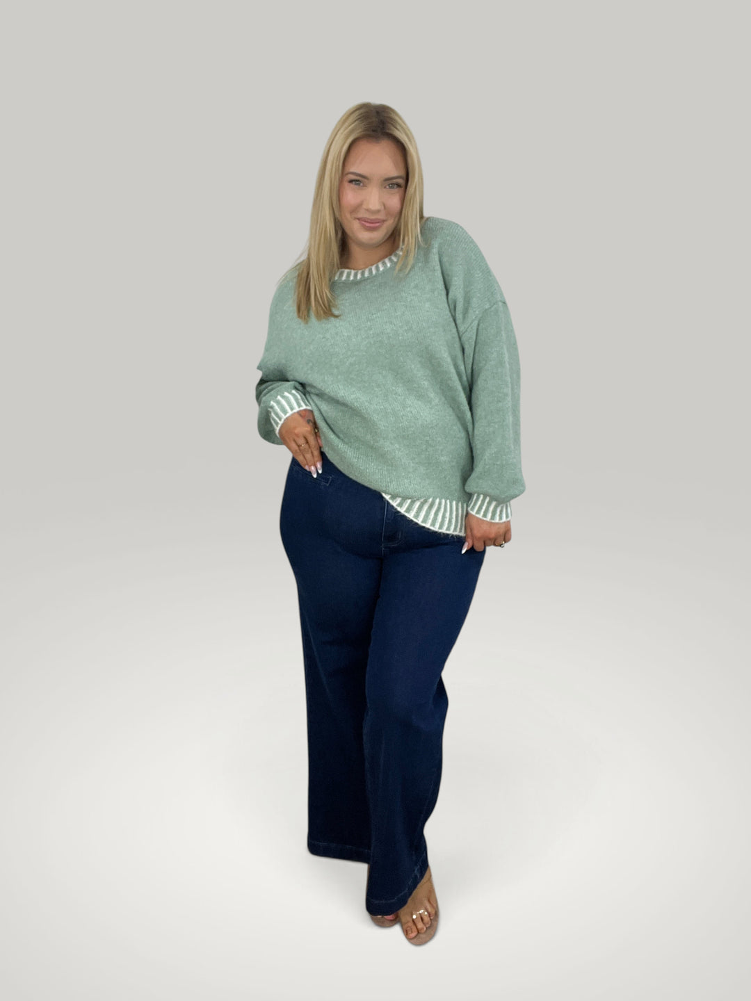 Modelo loira veste pulôver de malha verde Isabelle Hannover com gola redonda e punhos listrados em contraste