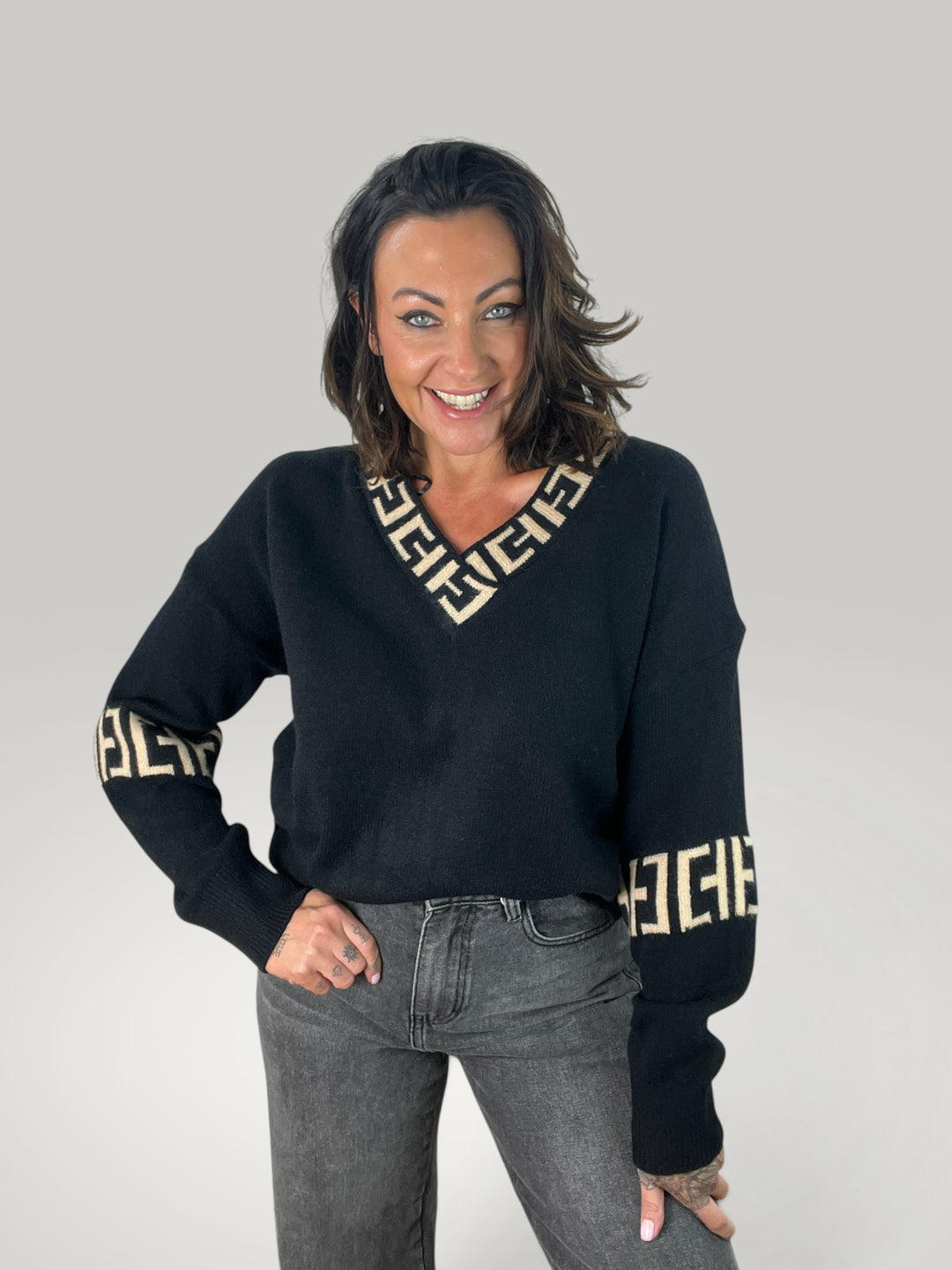Isabelle Hannover pulôver preto com decote em V e detalhes geométricos bege nas mangas e gola em modelo sorridente