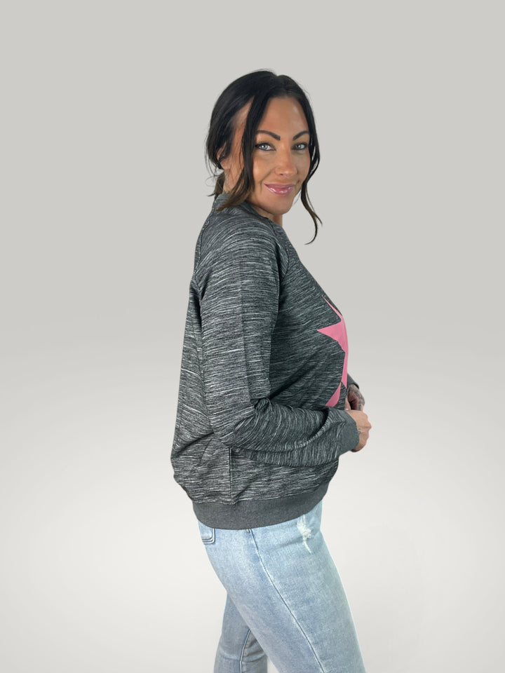 Modelo veste Isabelle Hannover sweatshirt cinzento com estampado de estrela rosa, corte largo e gola redonda.